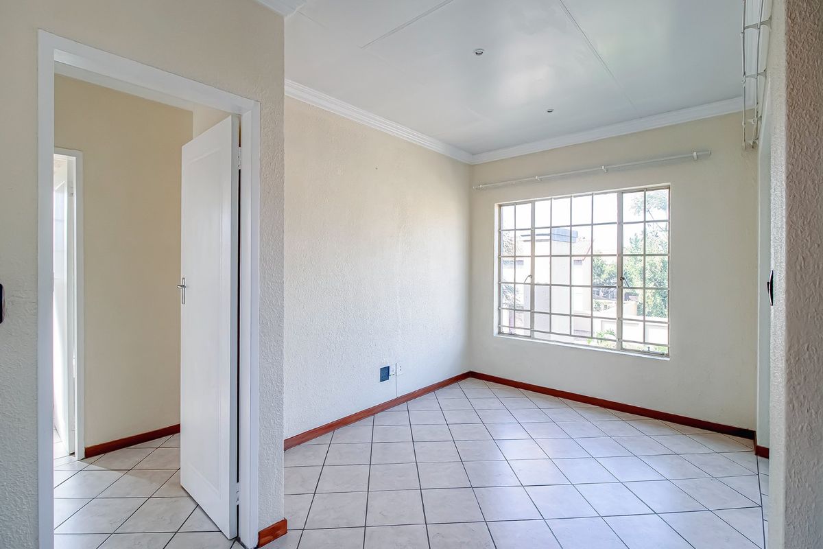 A bright, empty bedroom featuring neutral walls, tiled flooring, and a large steel-framed window providing natural light.