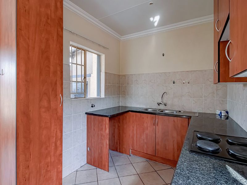 A functional kitchen featuring laminate cabinetry, granite countertops, a double bowl sink, and an integrated electric hob with tiled backsplash and flooring.