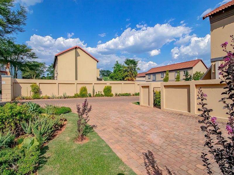 A well-maintained paved driveway entrance featuring a perimeter wall, pedestrian gate, and established landscaped garden beds.