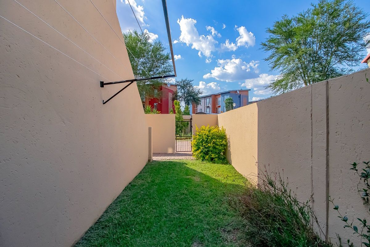 A private rear garden area featuring a small lawn, paved pathway, secure metal gate, and perimeter boundary walls with an attached washing line.