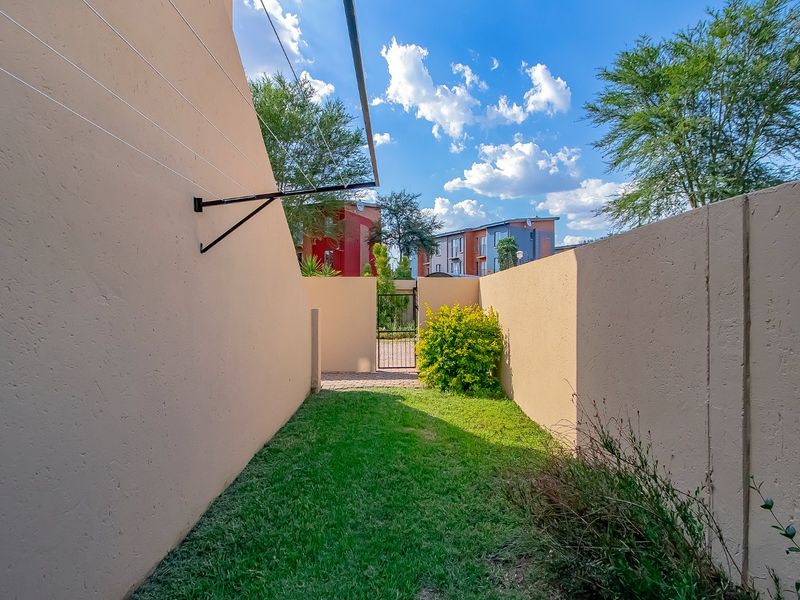 A private rear garden area featuring a small lawn, paved pathway, secure metal gate, and perimeter boundary walls with an attached washing line.