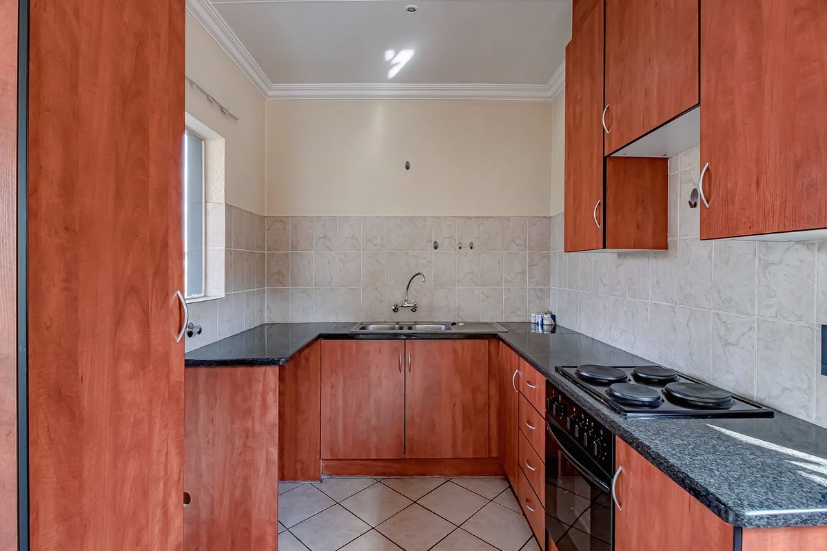 A functional kitchen featuring wood-finish cabinetry, granite countertops, a built-in oven with electric hob, and neutral tiled backsplash and flooring.