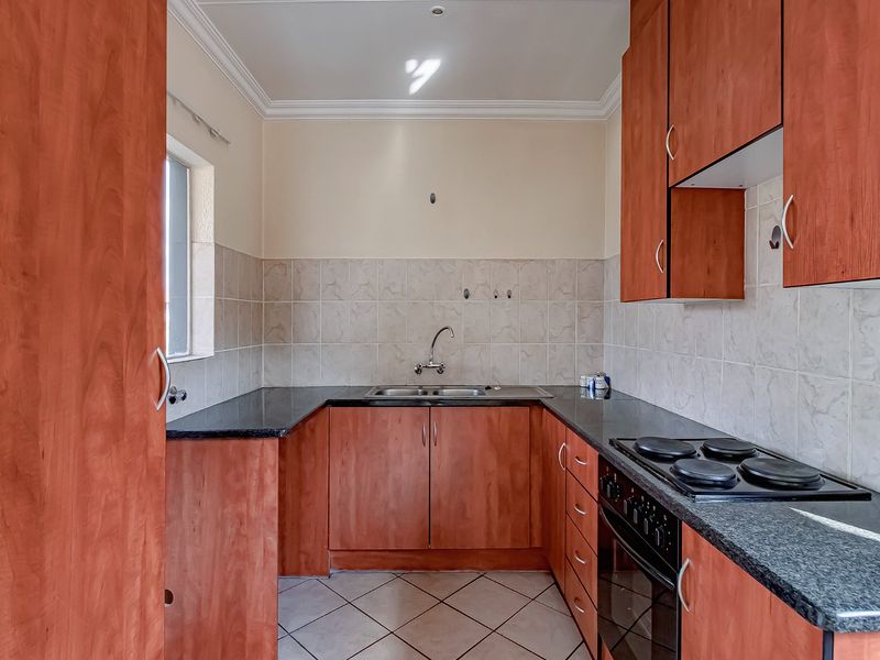 A functional kitchen featuring wood-finish cabinetry, granite countertops, a built-in oven with electric hob, and neutral tiled backsplash and flooring.