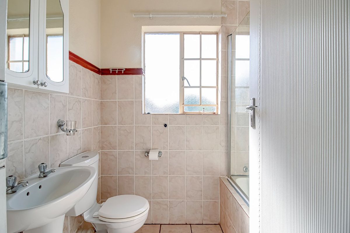 A functional bathroom featuring a pedestal basin, toilet, and a shower enclosure with tiled walls and flooring.