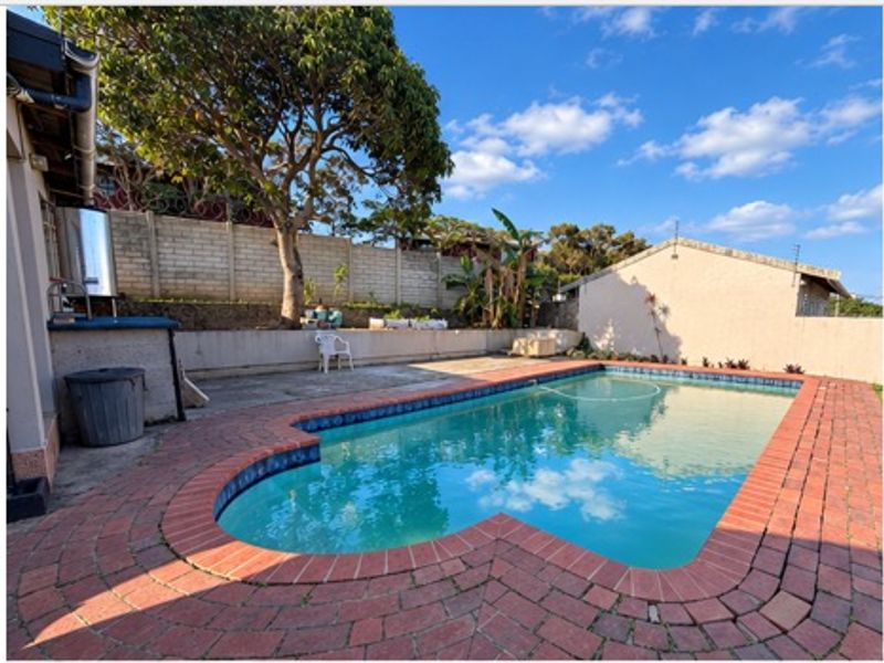 Outdoor pool area featuring a swimming pool with brick paving, a retaining wall, and a water tank set against a concrete boundary wall.