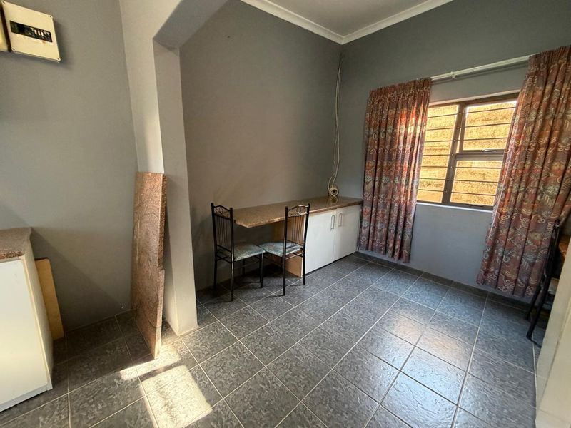 A kitchen area featuring tiled flooring, built-in cabinetry with granite countertops, and security burglar bars on the window.