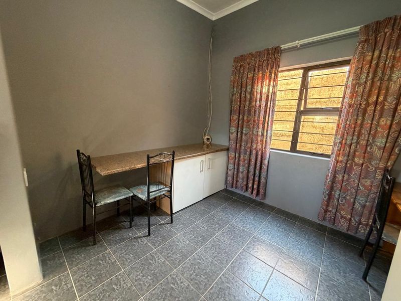 A bedroom featuring tiled flooring, a built-in desk with cabinetry, and a window fitted with security bars.