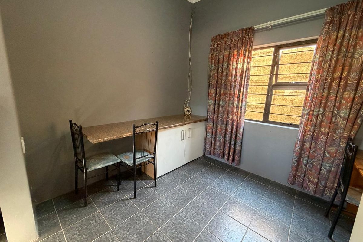 A bedroom featuring tiled flooring, a built-in desk with cabinetry, and a window fitted with security bars.