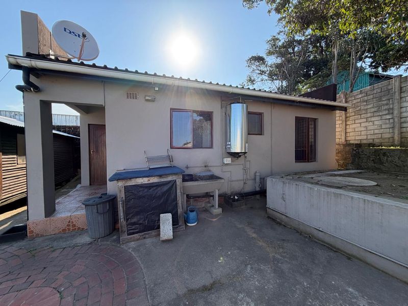 Rear exterior view of the townhouse featuring a paved patio area, external laundry sink, and wall-mounted electric geyser.