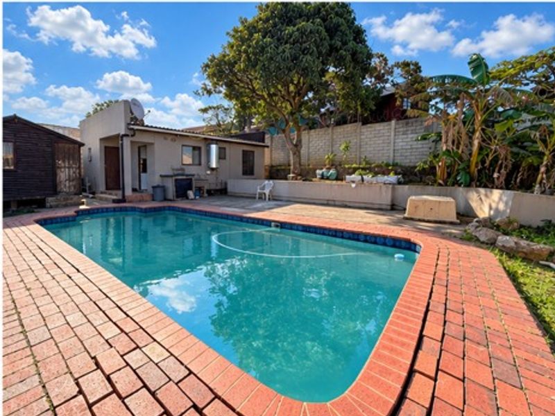 Outdoor pool area featuring a swimming pool with brick paving surround and a concrete patio area, set against a retaining wall.
