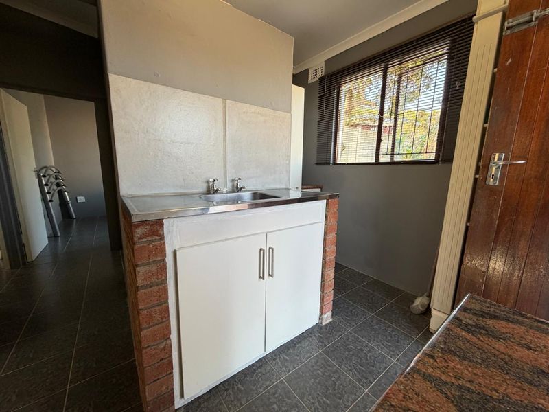A functional scullery area featuring a stainless steel sink, brick-based cabinetry, and tiled flooring, offering a practical space for utility and prep work.