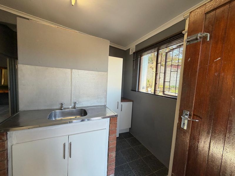 A functional laundry area featuring a stainless steel sink, built-in cabinetry, and tiled flooring, providing a practical space for utility needs.