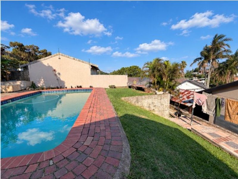 Outdoor pool area featuring a swimming pool with brick coping, a grassed lawn, and a retaining wall in a residential townhouse setting.