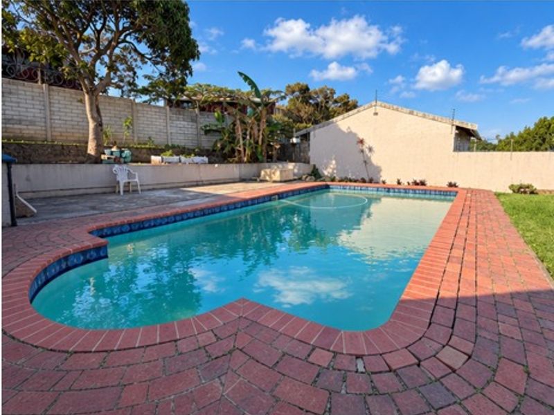 Outdoor swimming pool area featuring brick paving surround, retaining walls, and perimeter fencing in a private backyard setting.