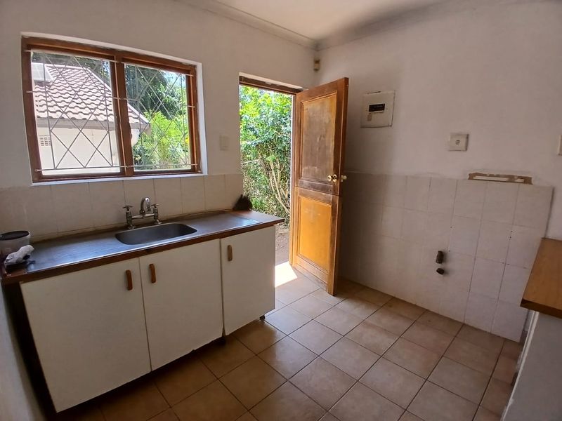A functional kitchen area featuring a stainless steel sink, tiled splashbacks, and direct access to the exterior, offering a blank canvas for renovation.
