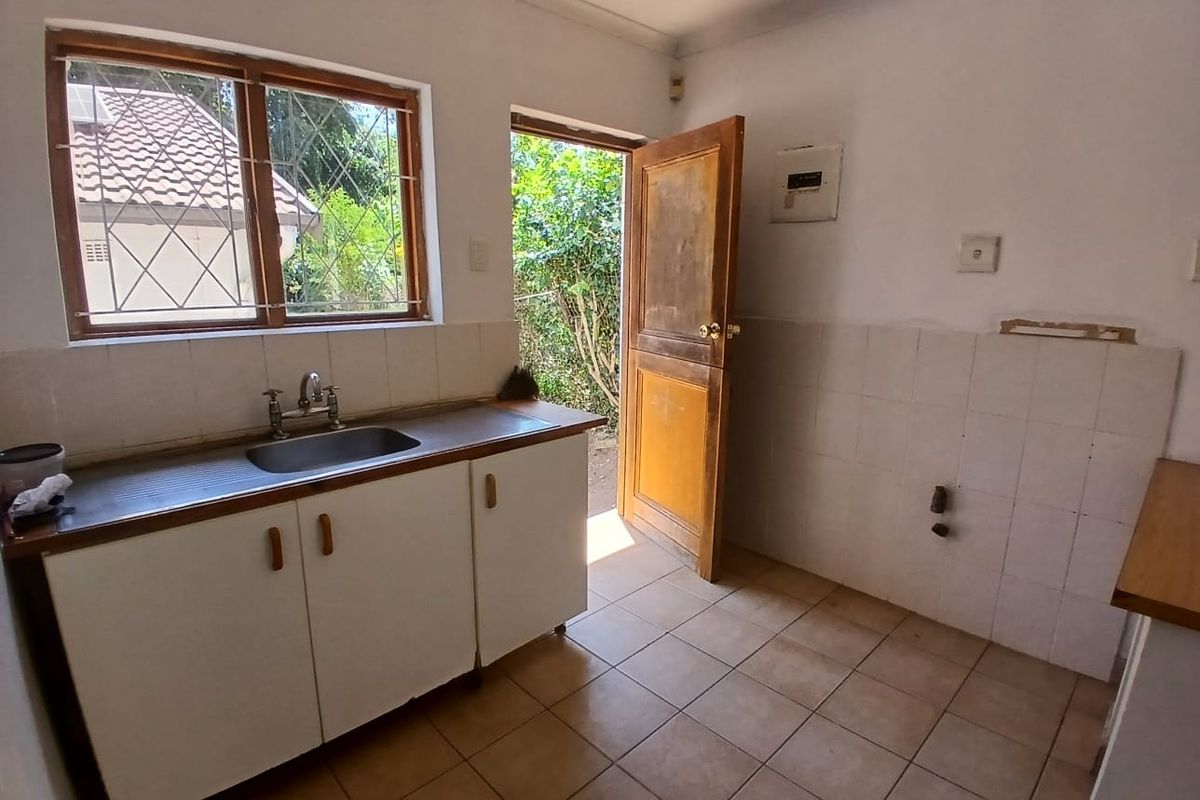 A functional kitchen area featuring a stainless steel sink, tiled splashbacks, and direct access to the exterior, offering a blank canvas for renovation.
