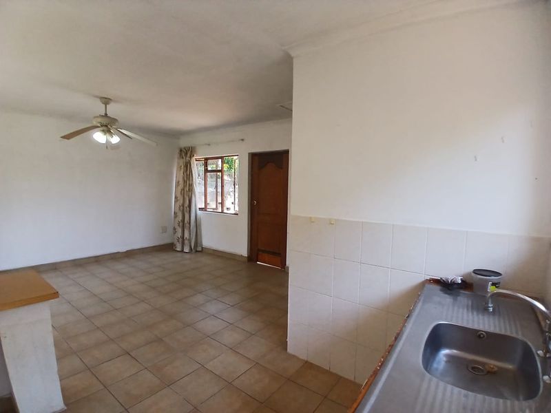 Open plan living area featuring tiled flooring, a ceiling fan, and a functional kitchen sink area with tiled splashback.