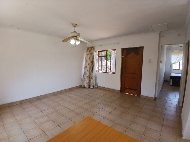 An empty living room featuring tiled flooring, a ceiling fan, and a wooden door, offering a blank canvas for interior design.