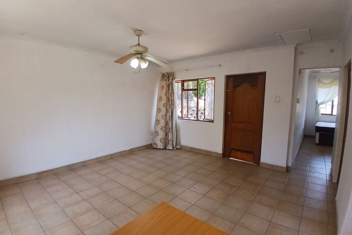 An empty living room featuring tiled flooring, a ceiling fan, and a wooden door, offering a blank canvas for interior design.