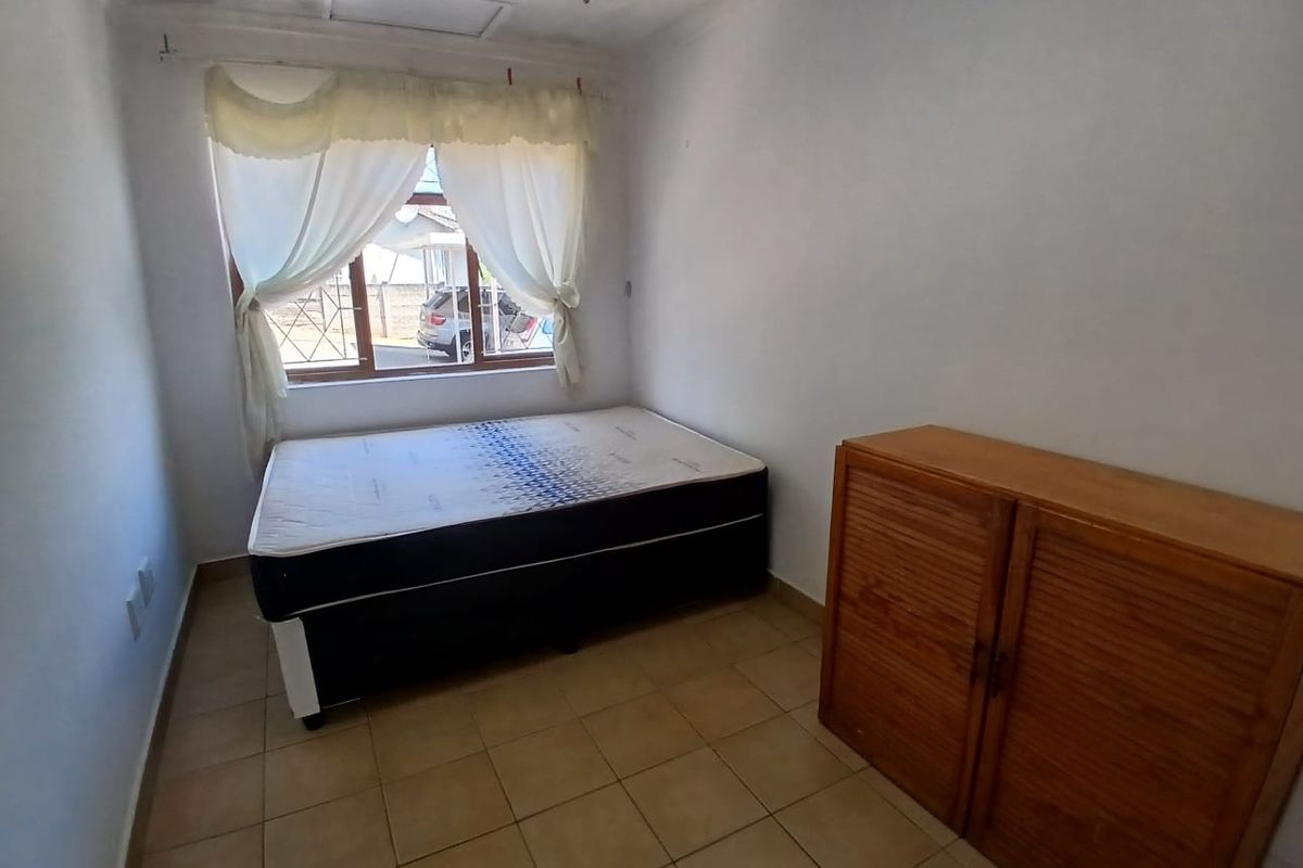 A simple bedroom featuring tiled flooring, a ceiling fan, and a window fitted with security bars.