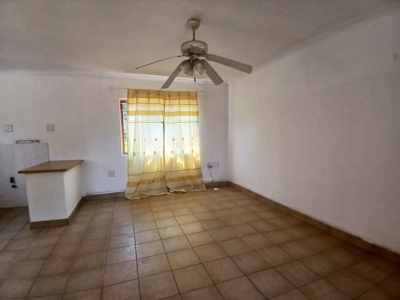 An empty open-plan living area featuring tiled flooring, a ceiling fan, and a built-in breakfast counter, offering a blank canvas for renovation.