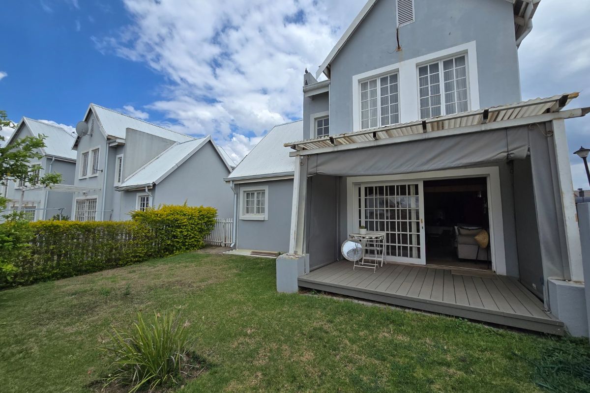Rear view of the house featuring a timber deck, retractable awning, and sliding glass doors leading into the living area, set within a private garden.