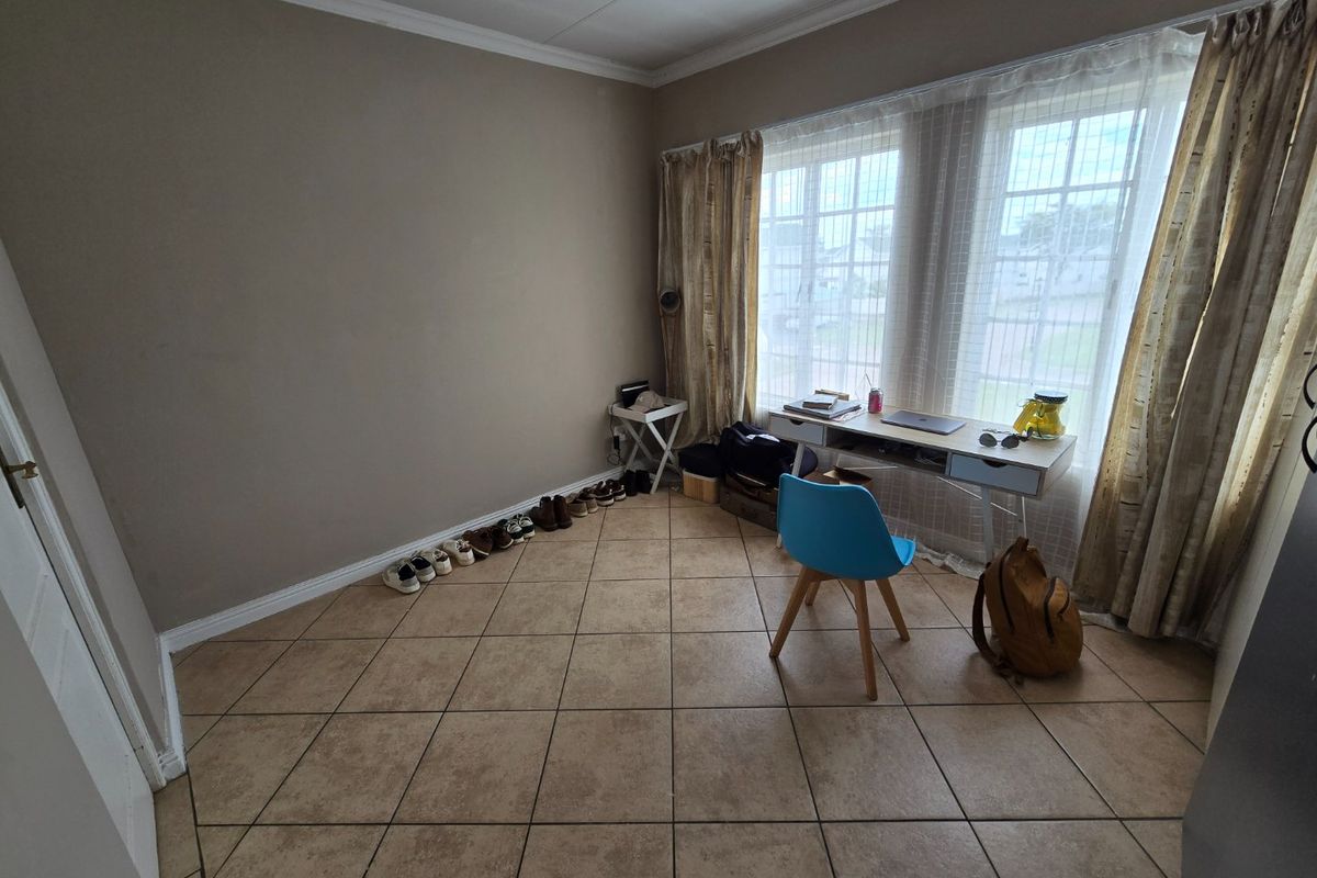 A bedroom featuring tiled flooring, cove cornicing, and large windows fitted with security bars, offering a functional space with neutral wall tones.