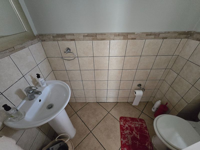A functional guest bathroom featuring a pedestal basin, tiled walls with a decorative border, and standard ceramic floor tiles.