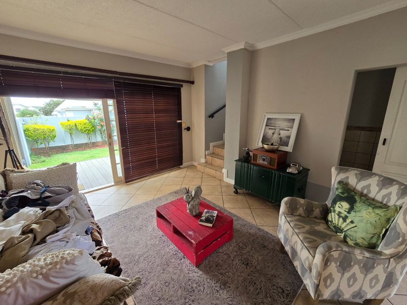 A living room featuring tiled flooring, a staircase, and large sliding glass doors that provide direct access to the outdoor patio and garden area.
