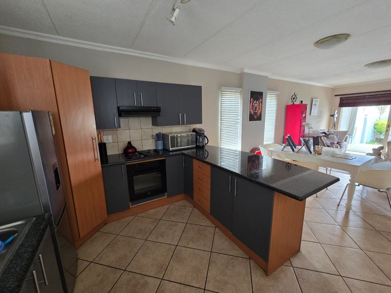 Open-plan kitchen and dining area featuring granite countertops, built-in oven, hob, extractor fan, and tiled flooring, flowing into a bright living space.