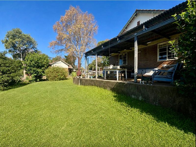A rear view of the property featuring a covered patio area with a concrete base, brick exterior walls, and a spacious lawn.