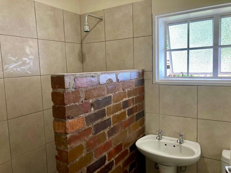 Bathroom featuring a unique exposed brick shower partition, pedestal basin, and tiled walls, currently requiring cosmetic updates and finishing touches.
