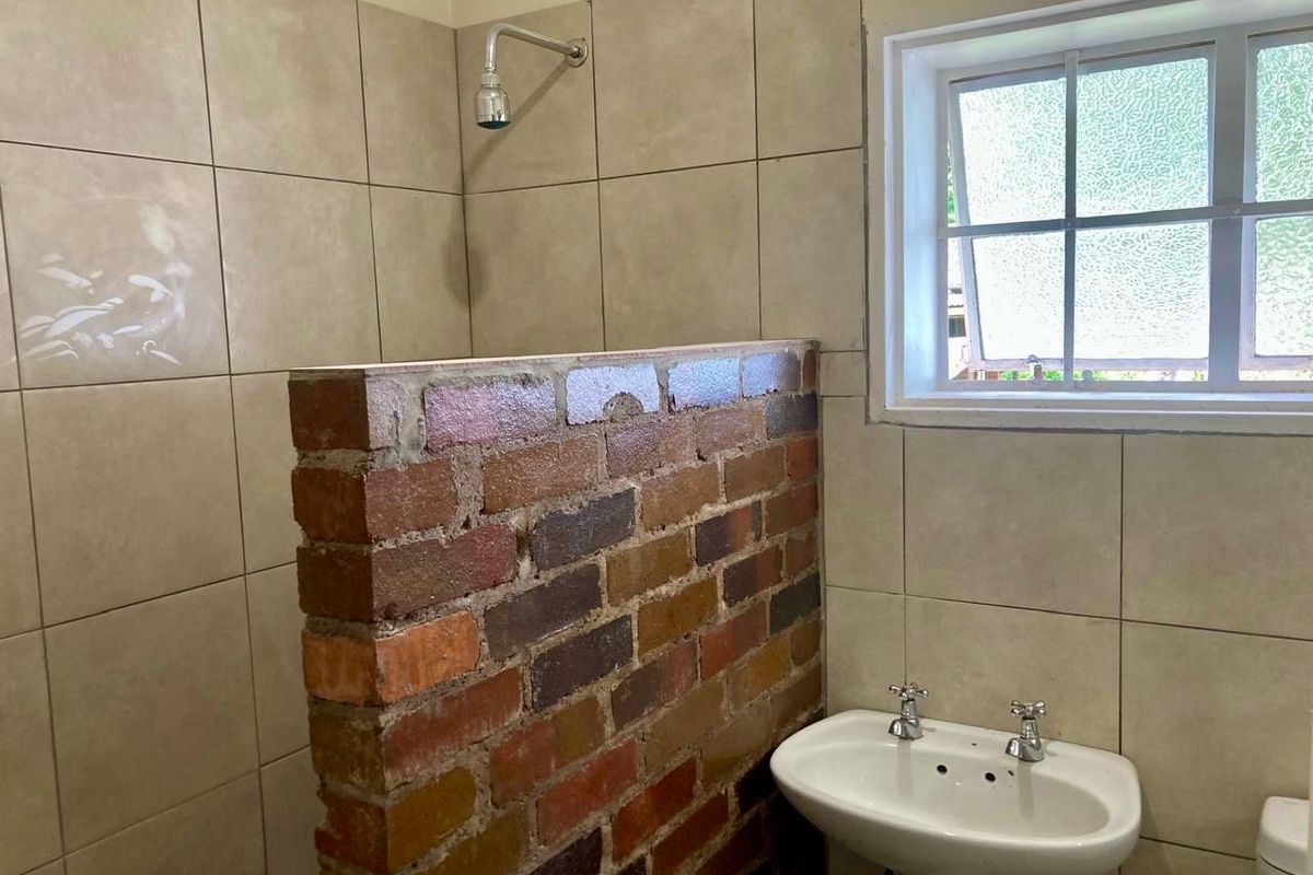 Bathroom featuring a unique exposed brick shower partition, pedestal basin, and tiled walls, currently requiring cosmetic updates and finishing touches.