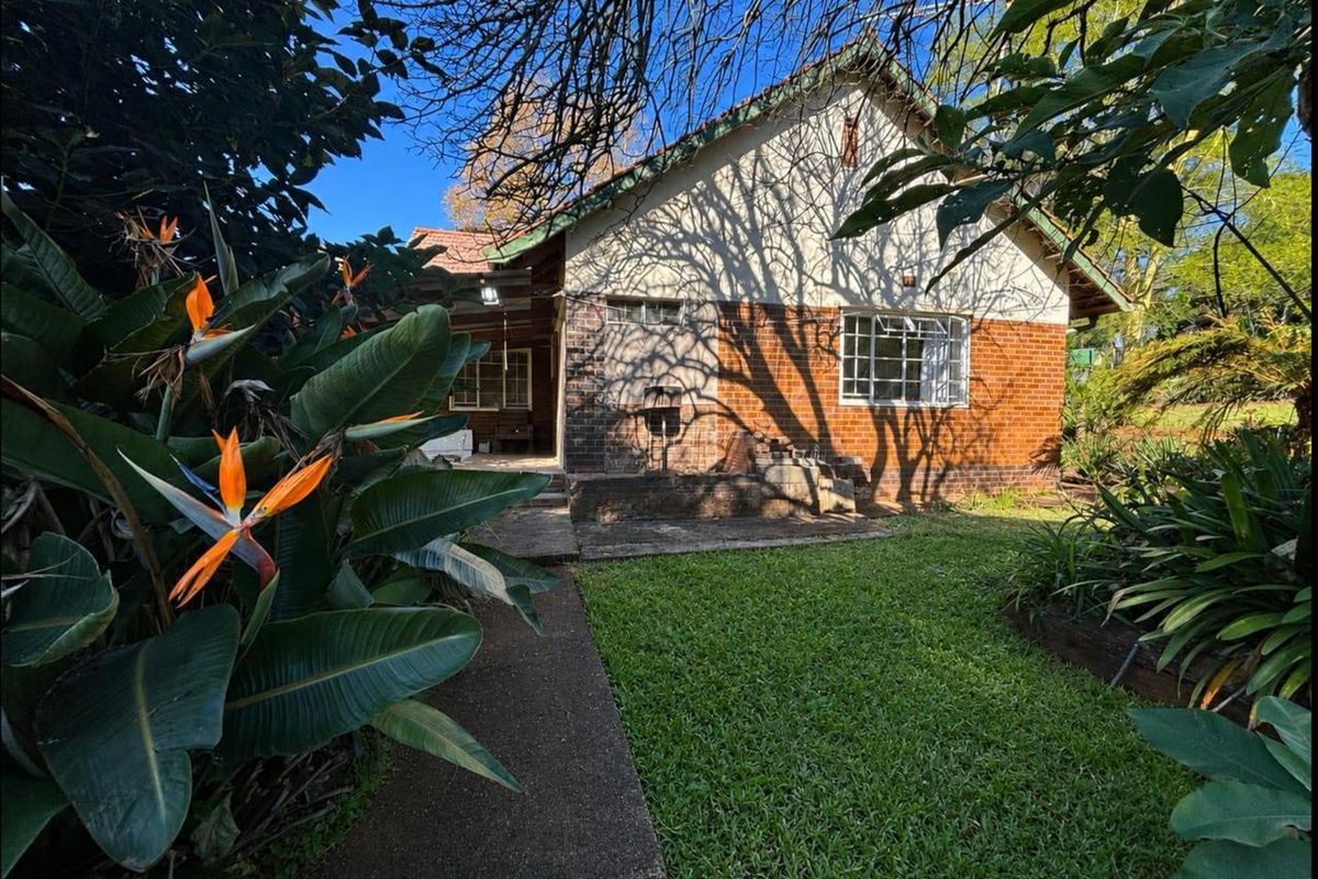 Rear view of the house featuring a brick facade, concrete pathway, and established garden area with mature trees.
