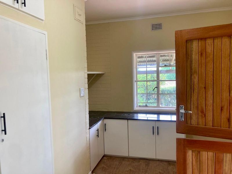 A functional scullery or utility area featuring white built-in cabinetry, dark stone countertops, and a timber door, offering practical storage and workspace.