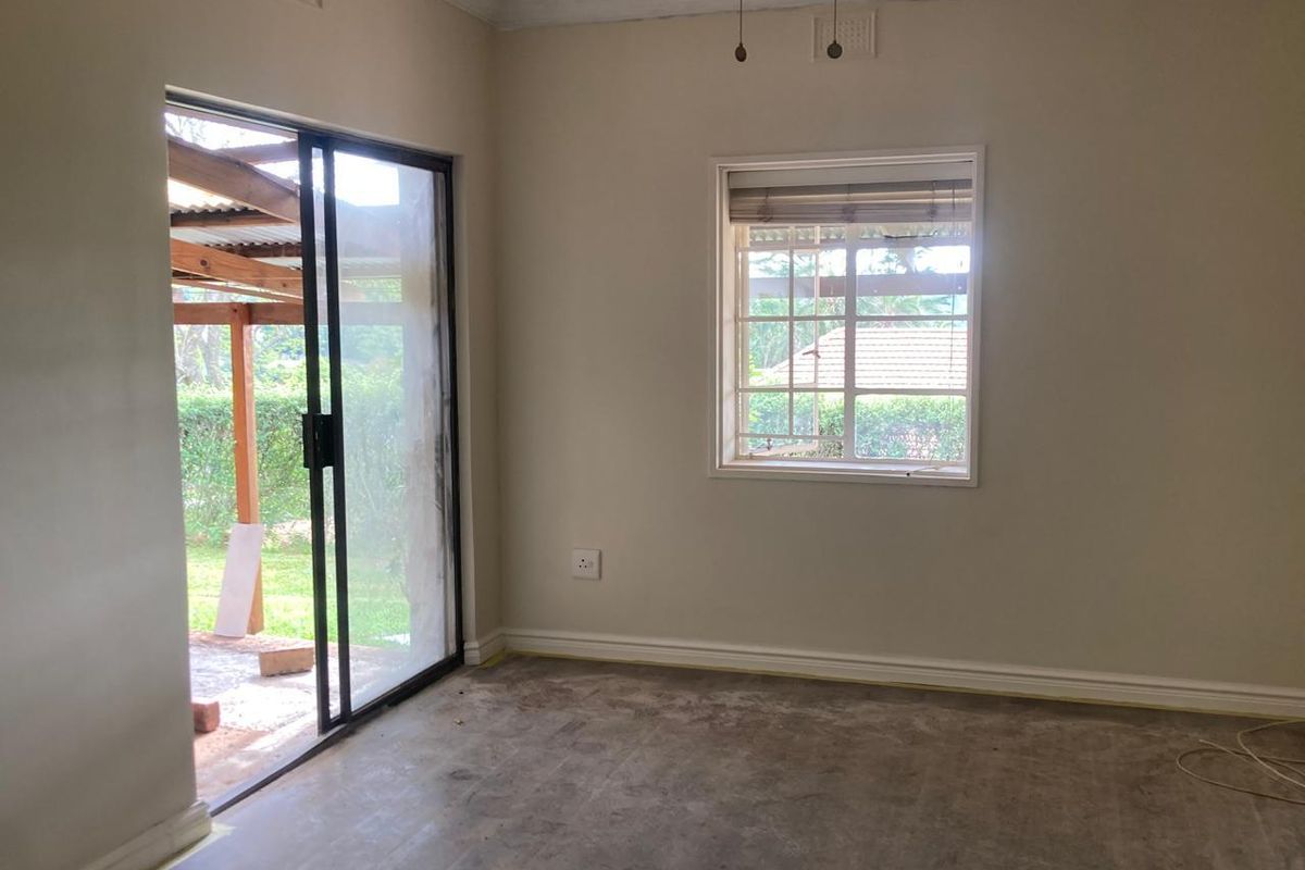 An empty living room featuring a sliding glass door leading to a patio and a window with security bars, awaiting new flooring installation.