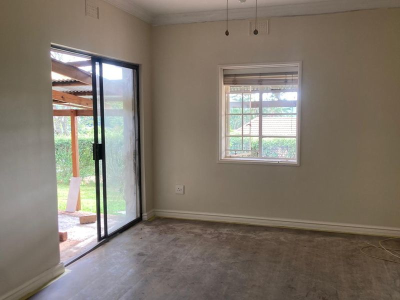 An empty living room featuring a sliding glass door leading to a patio and a window with security bars, awaiting new flooring installation.