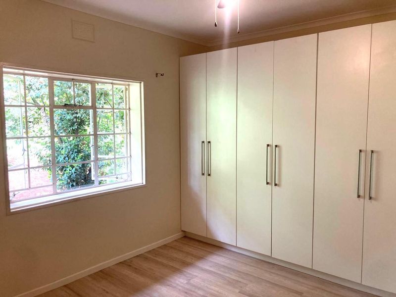 A bright, empty bedroom featuring modern laminate flooring and extensive floor-to-ceiling built-in cupboards, offering ample storage space.