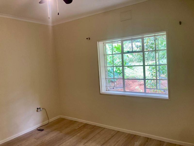 A vacant bedroom featuring laminate flooring, a ceiling fan, and a window with security bars overlooking the garden.
