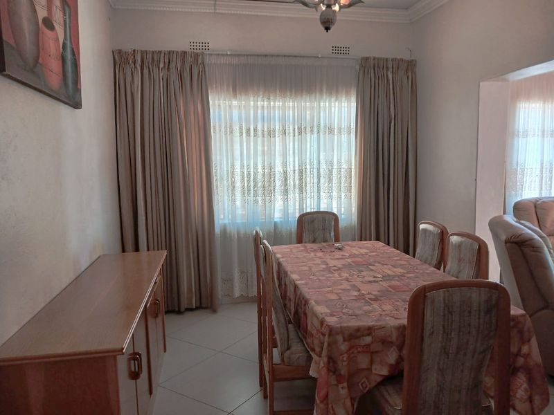 A dining room featuring tiled flooring, decorative ceiling cornicing, and a large window with curtains, providing a functional space for family meals.