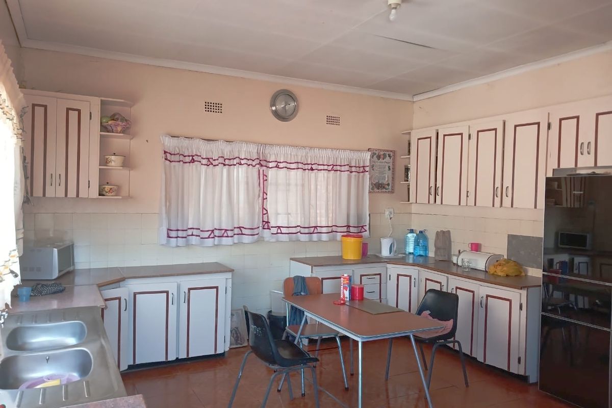 A dated kitchen featuring original built-in cabinetry, a double bowl stainless steel sink, and tiled finishes, offering significant potential for a modern renovation.