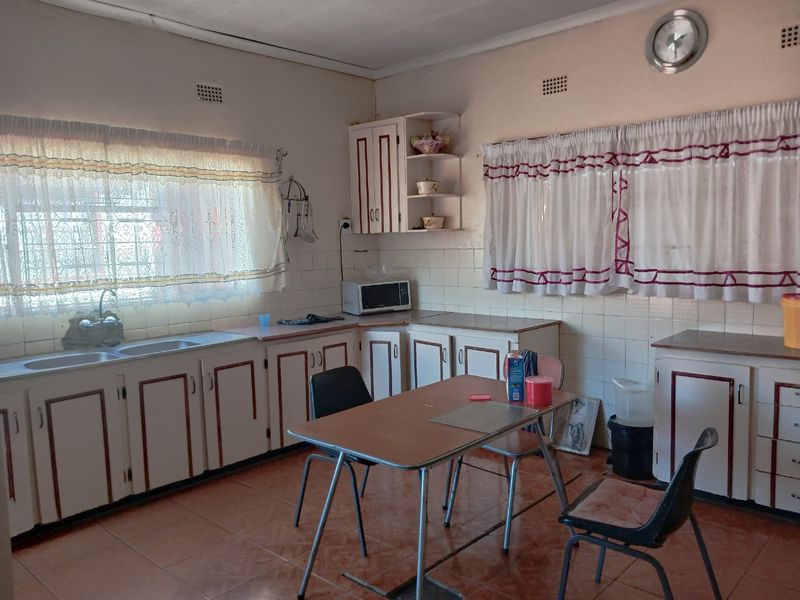 A dated kitchen featuring original cabinetry, tiled backsplash, and double sink, offering significant potential for modernization and renovation.
