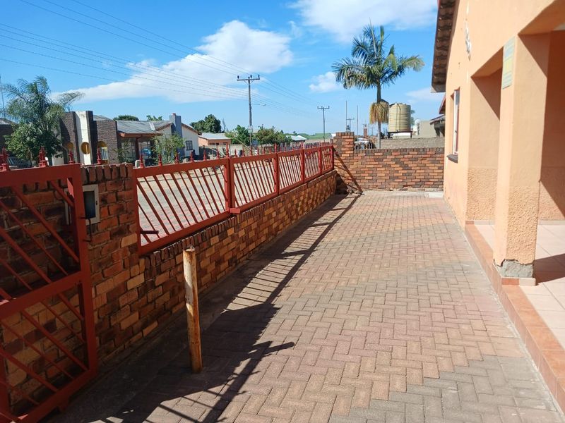 A paved front exterior area featuring a brick boundary wall with integrated metal security fencing and a gated entrance.