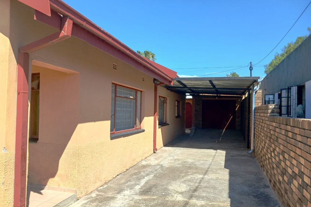 Rear exterior view showing a concrete driveway, carport structure, and brick boundary wall along the side of the house.
