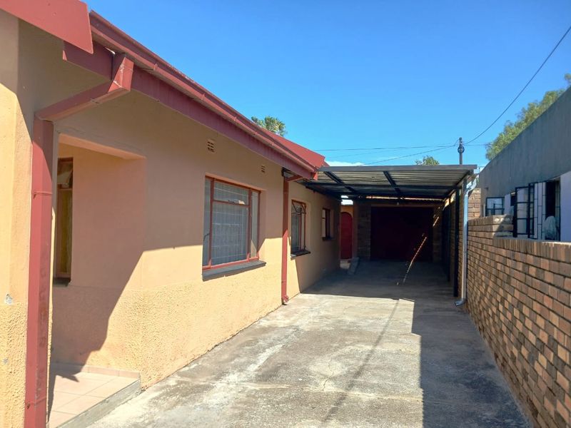Rear exterior view showing a concrete driveway, carport structure, and brick boundary wall along the side of the house.