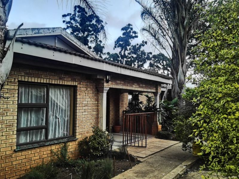 Front exterior view of a face brick house featuring a covered entrance porch, tiled roof, and a concrete walkway surrounded by established garden greenery.