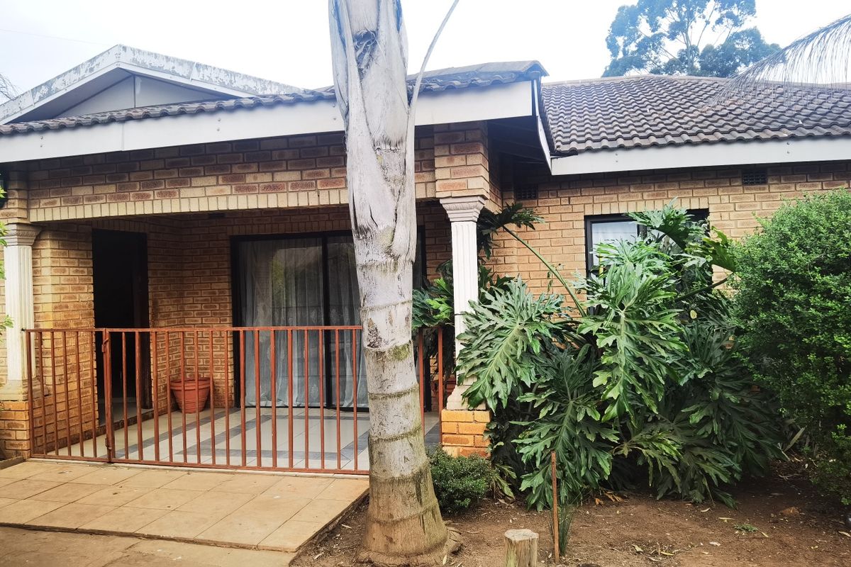 A rear view of the house featuring a covered patio with tiled flooring, brick facade, and sliding glass door access.