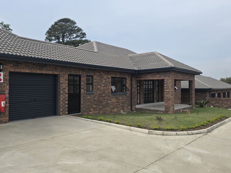 A well-maintained face brick townhouse featuring a tiled roof, a roller garage door, and a covered patio area with a concrete driveway.