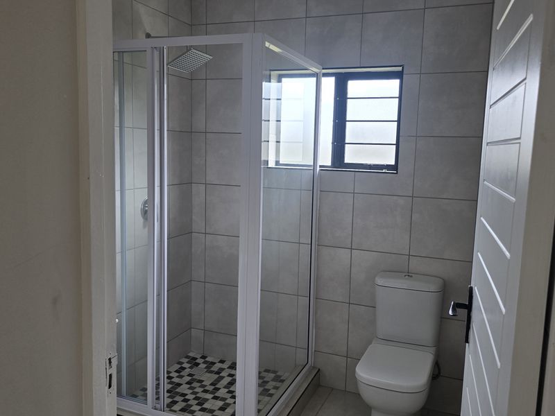 A clean, modern bathroom featuring a glass-enclosed shower with a rain shower head, a white toilet, and neutral wall tiling.