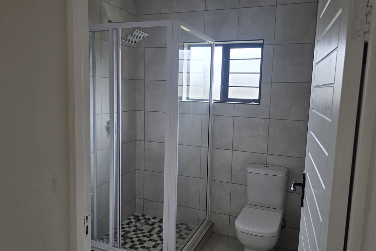A clean, modern bathroom featuring a glass-enclosed shower with a rain shower head, a white toilet, and neutral wall tiling.